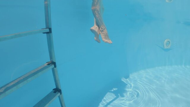 Female legs swinging under water in swimming pool.