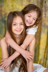 two little girls with long hair in white clothes cuddle. love between sisters. 