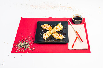 Portion of Japanese dumplings, gyozas, with red chopsticks, sesame and poppy seeds, soy sauce and red trivet with recycled paper napkin