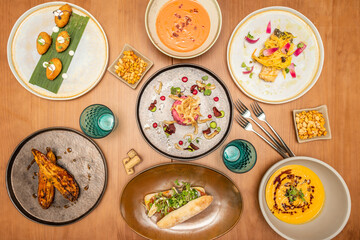 Set of tapas and elegant food plates with forks, salad with breaded prawns, boletus croquettes, roasted aubergines, anchovy sandwich, Andalusian gazpacho and Extremadura salmorejo