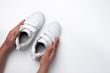 mock up two hands of a woman holding a child's white sneakers with velcro fasteners with a blank space for text isolated on a white background