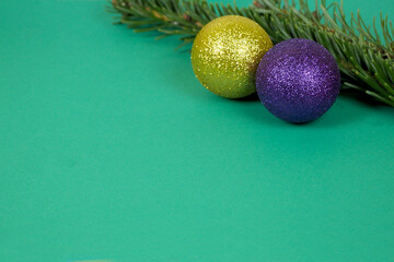 purple and yellow round shiny Christmas balls are lying next to a branch of a green Christmas tree on a green background . side view