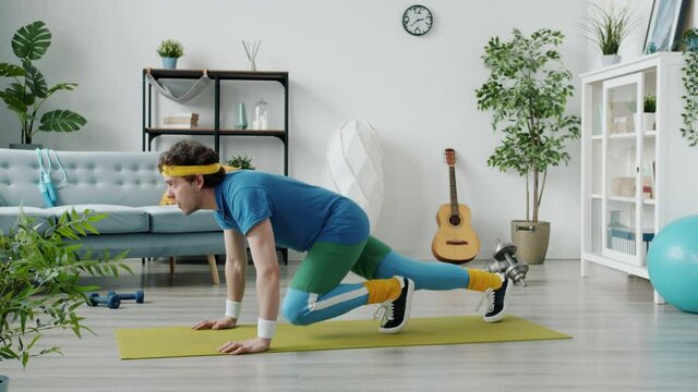 Slow motion of funny sportsman in colorful outfit training on mat then feeling tired exercising alone at home. Sports activities and apartment concept.