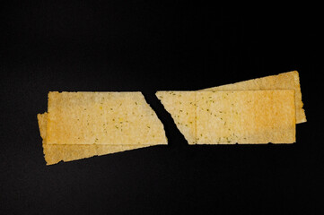 Broken potato long chips with dill on an isolated dark background. Top view.