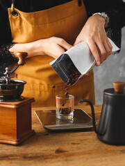 Barista pouring roasted coffee beans in cup to scale and measure