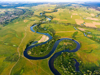 Aerial view of a curve river among fields and forests with town on the horizon and the beaches on the edges