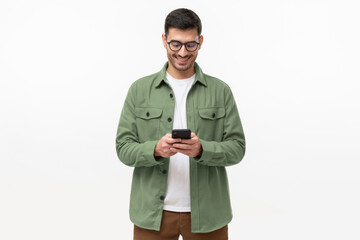 Young man in green casual shirt looking at phone, standing isolated on gray background