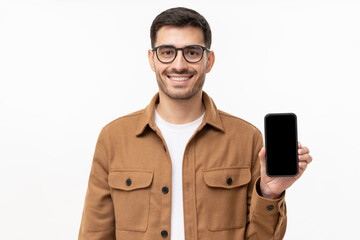Young smiling man in casual shirt showing blank screen smartphone in hand, isolated on gray background