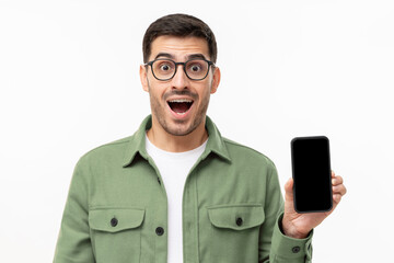 Surprised but excited man showing blank screen of his phone in hand, isolated on gray background