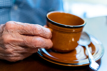 Closeup view of the old hands of an elder man taking a cup if coffee 