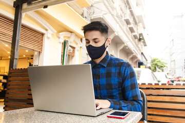 Handsome young man with face mask using his laptop in a public space.