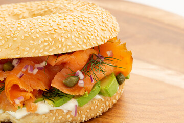 Closeup of smoked salmon bagel sandwich with cream cheese and avocado on wooden board