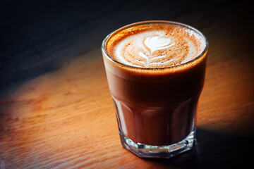 Flat-white coffee cup served on wooden table in spot of light, copyspace