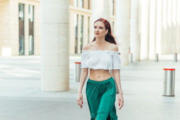 Beautiful red-haired woman in her thirties in a blouse and green skirt walks in the summer