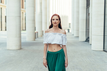 Confident redhead girl walks around the city in summer in light clothes