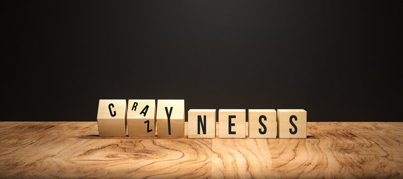 cubes with message CRAZYNESS on wooden base in front of a blackboard