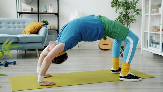 Sportsman in retro outfit is exercising in crab position on yoga mat training alone concentrated on sports activity. People and well-being concept.