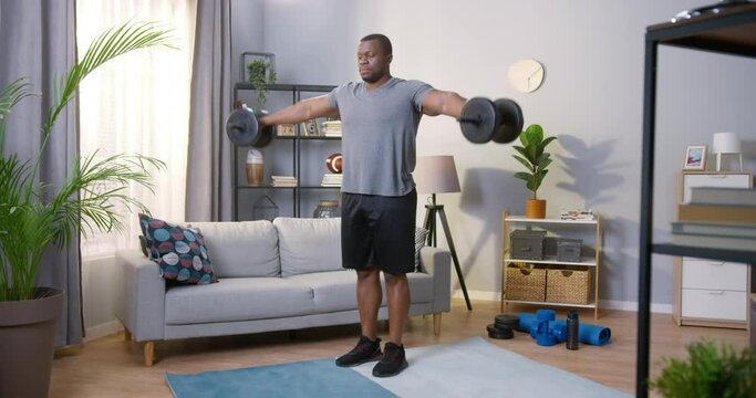 Full length view of the strong man lifting a dumbbell while having hard workout at home during the self isolation. Sport concept. Stock video