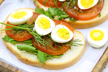 Fresh toast sandwiches with quail eggs, tomatoes and green herbs. Closeup. Top view. Copy space.