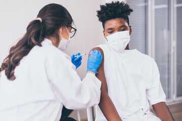 Naklejka premium African boy wearing face mask getting vaccinated during coronavirus or covid-19 pandemic at hospital,Vaccination concept