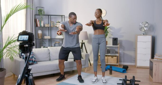 Do like this. Happy healthy young couple recording their video blog episode about healthy activities while standing at the mat at home and training