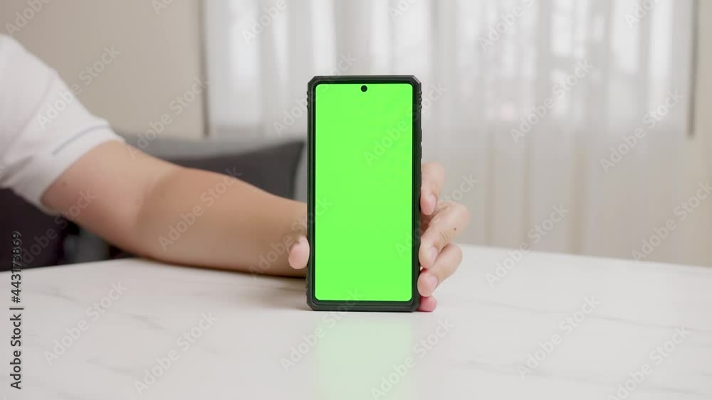 Poster man's hand shows mobile smartphone with green screen in vertical position isolated on green backgrou