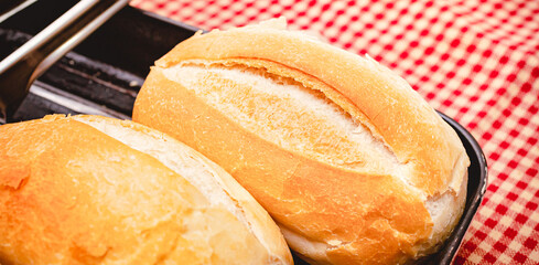 Pão francês. Dois pães franceses servidos em uma assadeira preta sobre uma mesa com toalha...