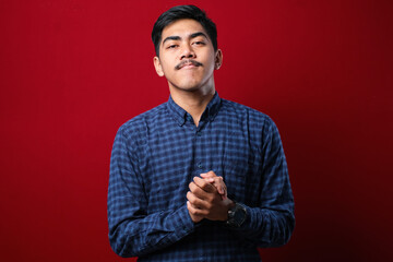 Fototapeta premium Young handsome man wearing casual shirt with hands together and crossed fingers smiling relaxed and cheerful. Success and optimistic
