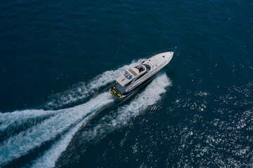 Luxury motor boat on dark blue water aerial view. The yacht is fast moving on dark water. Large white yacht on the water in motion top view.