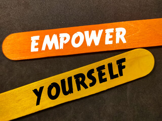 Text EMPOWER YOURSELF with colorful wooden stick on black background.