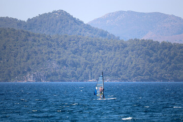 View to windsurfer in the sea and green mountains in mist. Water sports, beach vacation