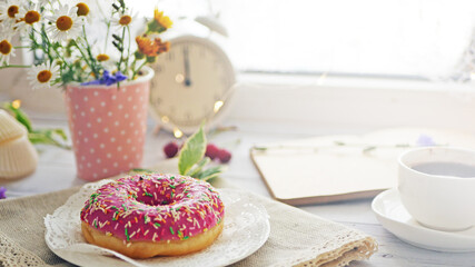 Donut in pink glaze on a background of wild flowers of chamomiles, fresh berries on a wooden table