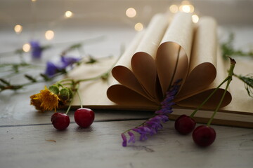 Book with folded sheets. Composition with an old book, wildflowers, berries, daisies on a wooden table. Background with a book