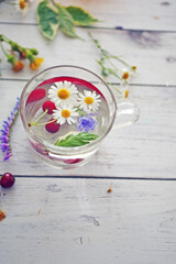 Obraz na płótnie Canvas Flower tea. Transparent mug with a drink with chamomile flowers and cherry berries on a wooden table