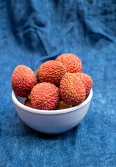 Closeup of Lychee or Litchi in a Bowl Isolated on Blue Fabric Background in Vertical Orientation