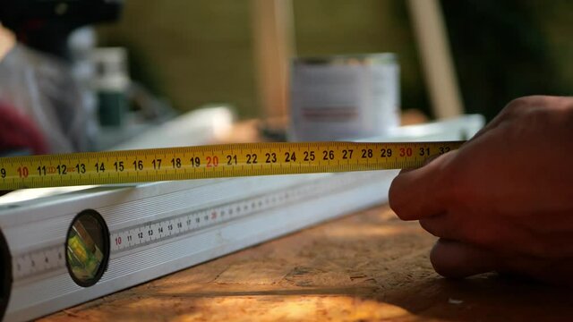 Man's hand holding tape measure above construction spirit bubble level tool, measuring the distance above plywood, close up
