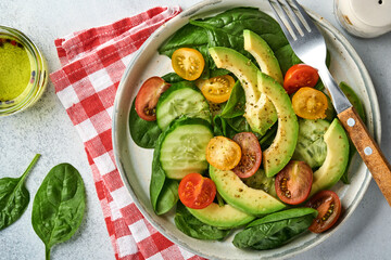 Avocado, red, yellow, black cherry tomato, spinach and cucumber fresh salad with spices pepper and olive oil in grey bowl on grey slate, stone or concrete background. Healthy food concept. Top view.
