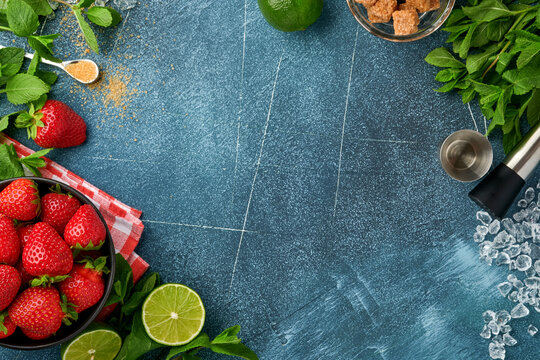 Food fresh ingredients for making lemonade, infused detox water or cocktail. Strawberries, lime, mint, basil, cane sugar,  ice cubes and shaker on dark blue stone or concrete background. Top view 