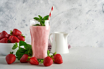 Strawberry smoothie or milkshake with berries and mint in tall glass on light grey background. Summer drink shake, milkshake and refreshment organic concept. Place for text.