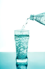 Pouring fresh water in glass from plastic bottle on blue background. Fresh drinking water glass with bubbles blue background.