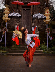 Woman dancing traditional Balinese dance in front of the temple. Caucasian woman wearing Balinese clothes. Culture and religion. Penjor bamboo and umbrella decoration. Penglipuran, Bali