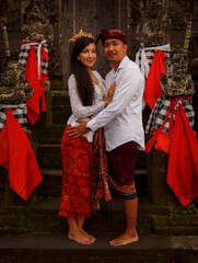 Multicultural couple standing near the temple in Bali. Caucasian wife and Balinese husband wearing traditional clothes. Culture and religion. Penglipuran, Bali