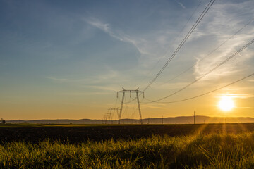 High voltage electric transmission towers and power lines at sunset.