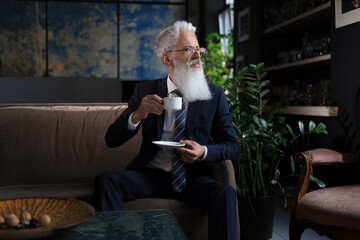 Handsome mature man holding coffee cup sitting on the sofa in office. Coffee break.