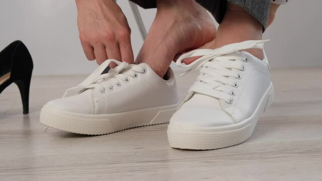 Close-up business woman takes off her shoes puts on white leather sneakers.