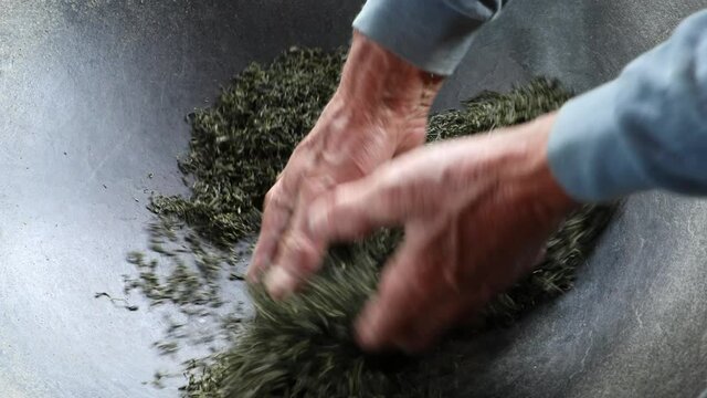 The process of making tea by hands, rubbing tea leaves in the wok with both hands, traditional Chinese method of frying tea leaves