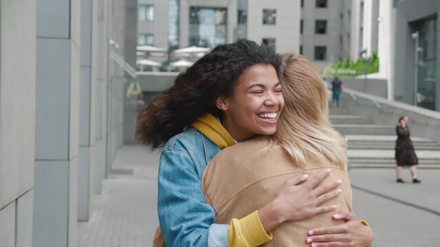 Two young women meeting and hugging on street