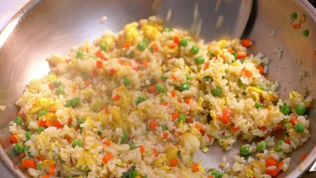 Close-up of egg fried rice with carrots and green peas, using spatula to stir-fry the rice in the wok