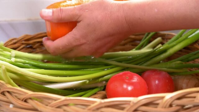 Closeup of washing the fresh vegetables with running water, garlic shoots, carrots, tomatoes in the basket