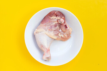 Raw chicken leg in white plate on yellow background